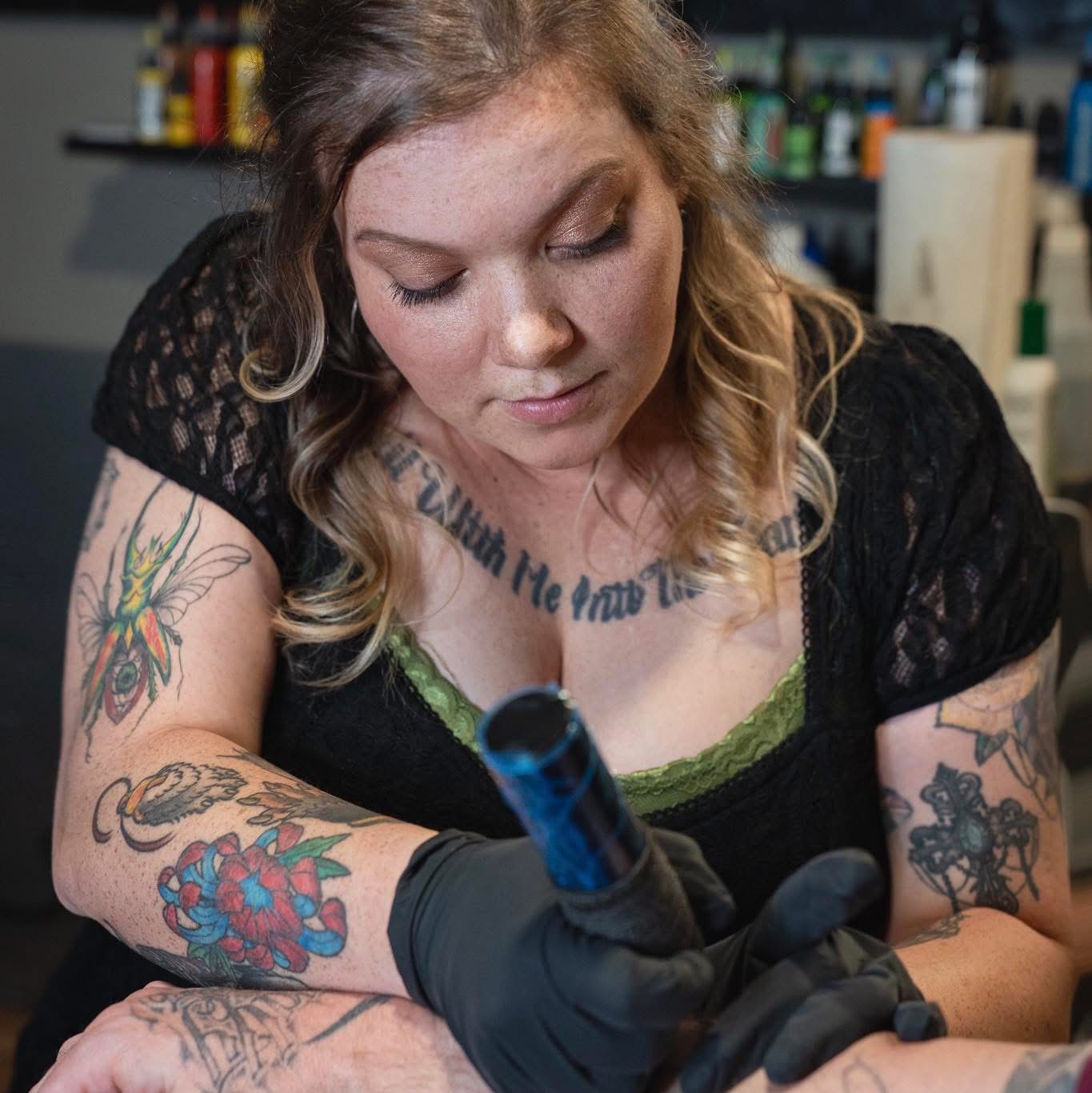 Ascended tattoo artist concentrating on a tattoo, wearing gloves and holding her tattoo machine
