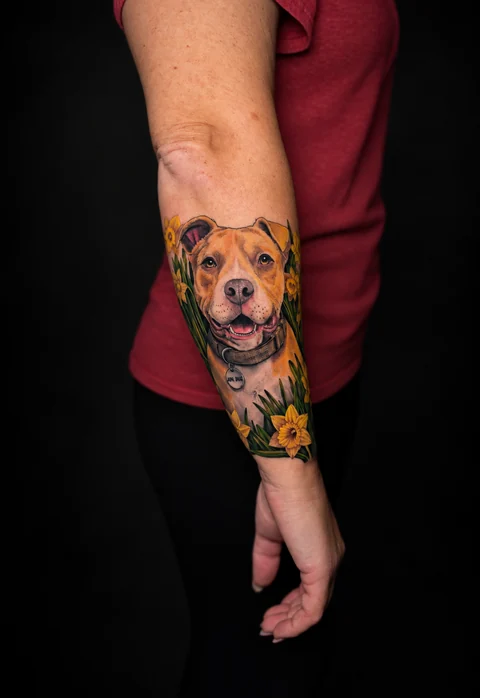 Color dog portrait surrounded by yellow daffodils on a forearm