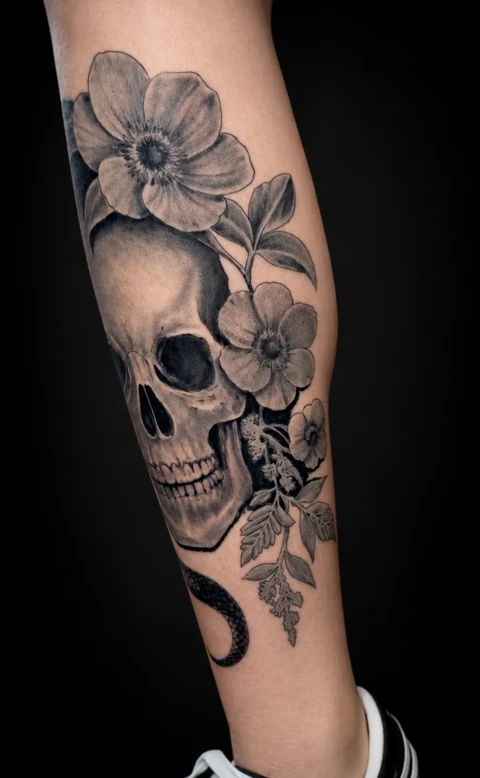 Black and gray skull and botanical calf tattoo, front angle
